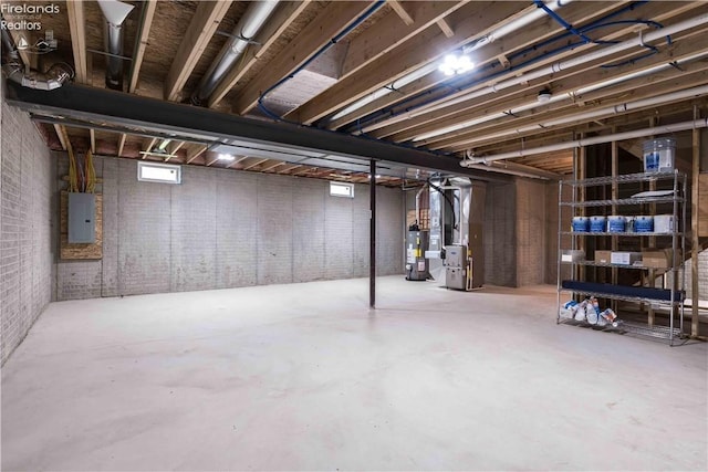 basement featuring water heater, brick wall, electric panel, and heating unit