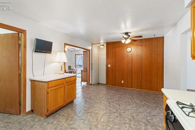 kitchen with ceiling fan, wooden walls, and gas stove