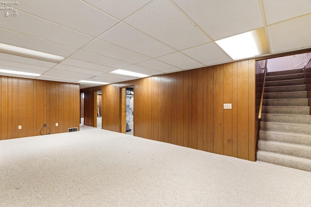 basement featuring a paneled ceiling and wood walls