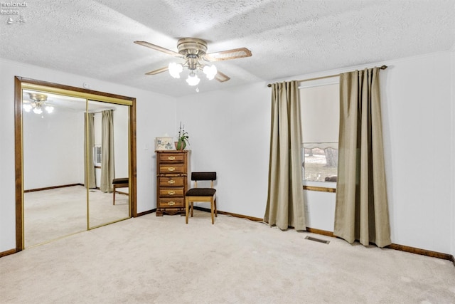 living area featuring light carpet, ceiling fan, and a textured ceiling