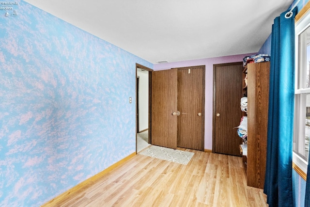 unfurnished bedroom with two closets and light hardwood / wood-style flooring