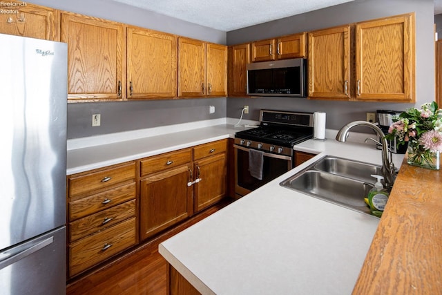 kitchen featuring stainless steel appliances, sink, a textured ceiling, and dark hardwood / wood-style flooring