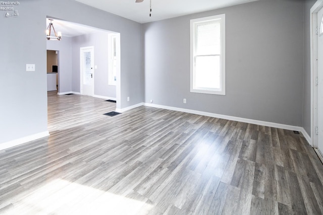 empty room with wood-type flooring and ceiling fan with notable chandelier