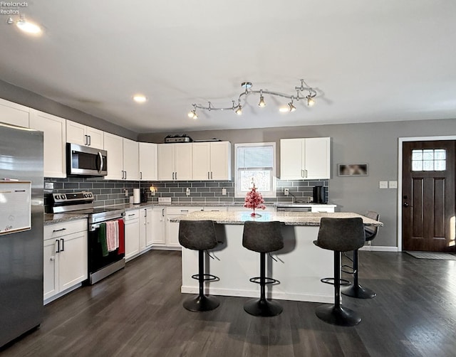 kitchen with appliances with stainless steel finishes, a kitchen breakfast bar, light stone countertops, white cabinets, and a center island