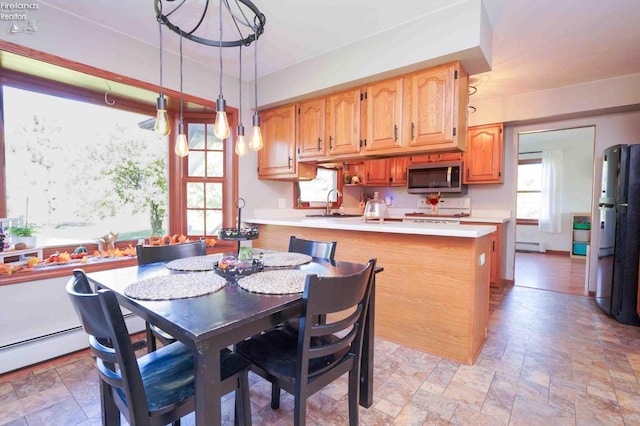 interior space featuring a baseboard radiator, decorative light fixtures, black refrigerator, sink, and a kitchen island with sink