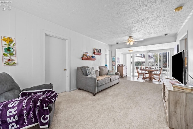 living room featuring ceiling fan, light colored carpet, a textured ceiling, and wooden walls