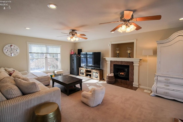 living room featuring ceiling fan, a tile fireplace, and light carpet