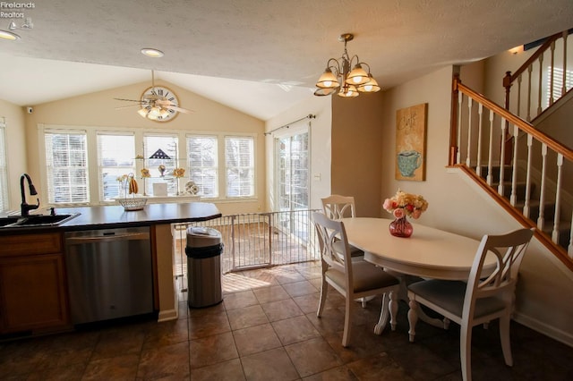 kitchen with dark tile patterned flooring, stainless steel dishwasher, sink, ceiling fan with notable chandelier, and lofted ceiling