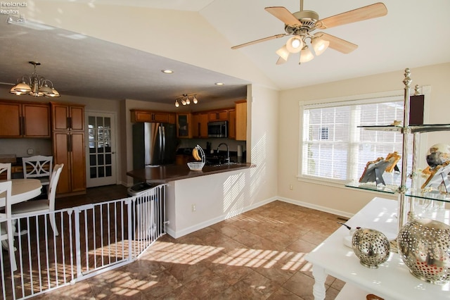 kitchen featuring ceiling fan with notable chandelier, decorative light fixtures, stainless steel appliances, sink, and vaulted ceiling