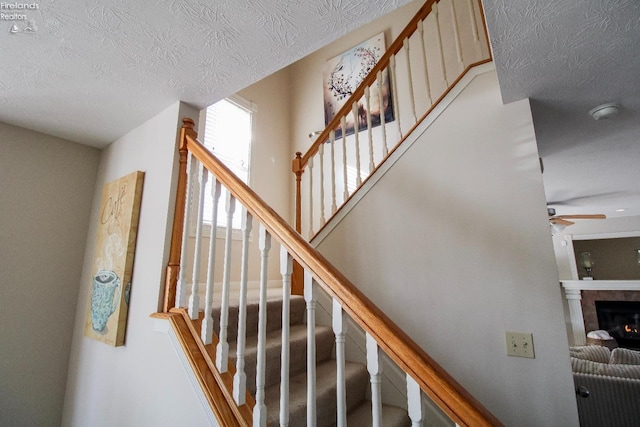 stairway featuring ceiling fan, a textured ceiling, and a tiled fireplace