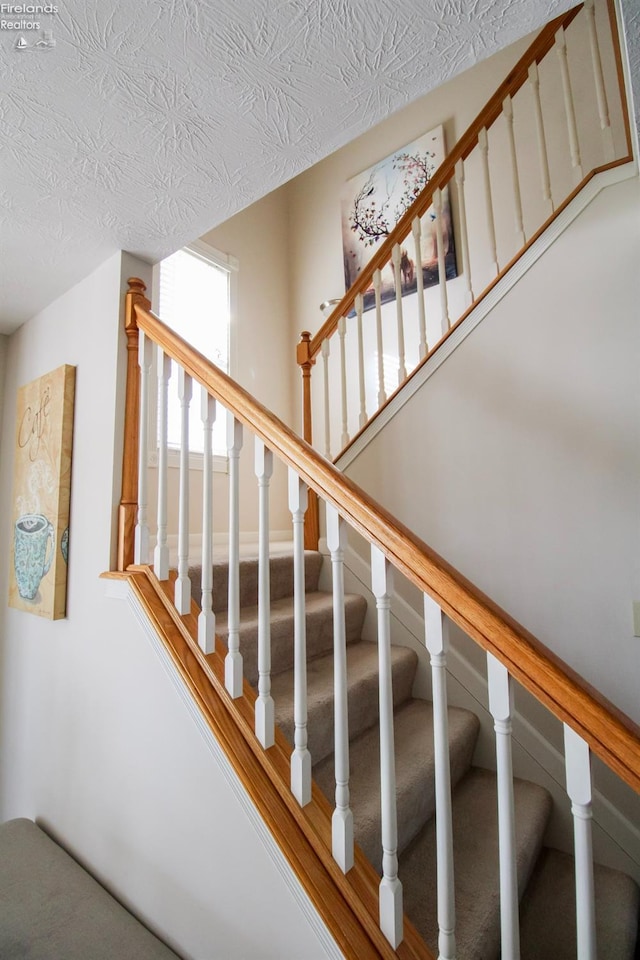 stairway with carpet floors and a textured ceiling