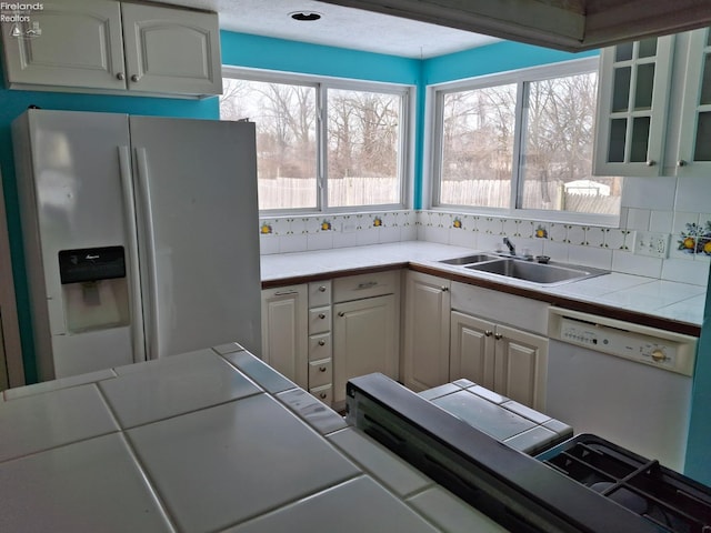 kitchen featuring sink, white appliances, white cabinets, and tile counters