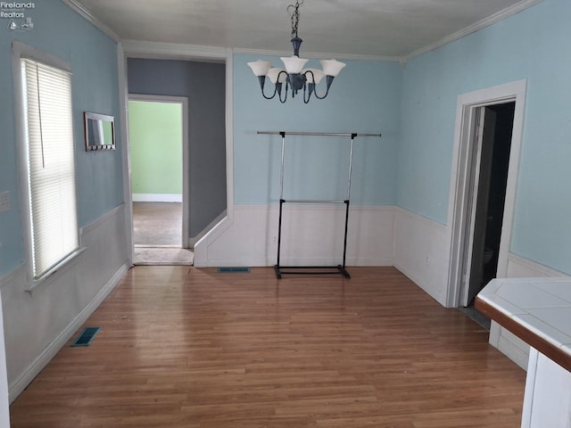 unfurnished dining area with ornamental molding, hardwood / wood-style floors, and an inviting chandelier