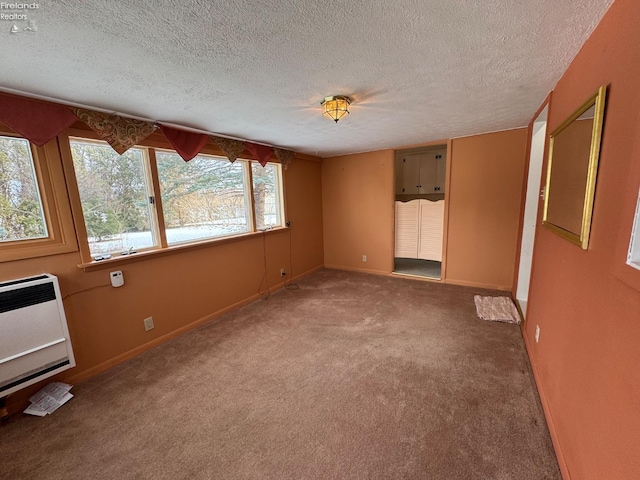 spare room featuring a textured ceiling, carpet floors, and heating unit