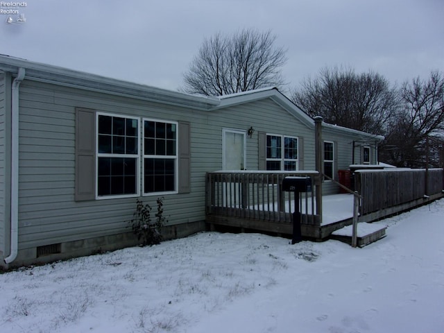 snow covered back of property with a deck