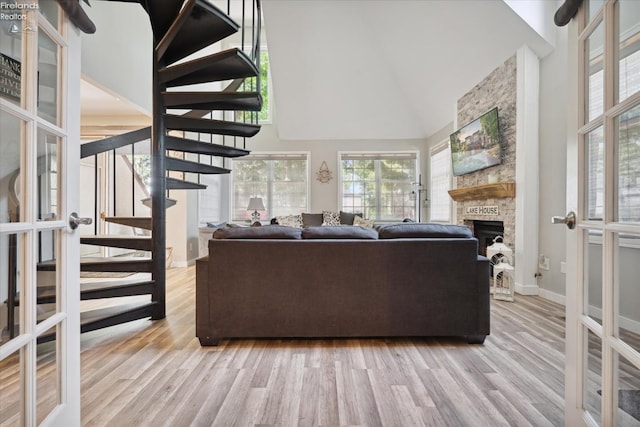 living room featuring a high ceiling, a stone fireplace, french doors, and light hardwood / wood-style flooring