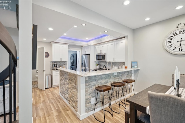 kitchen with appliances with stainless steel finishes, kitchen peninsula, a raised ceiling, light hardwood / wood-style floors, and white cabinets