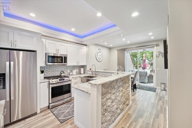 kitchen featuring sink, light stone counters, kitchen peninsula, stainless steel appliances, and white cabinets