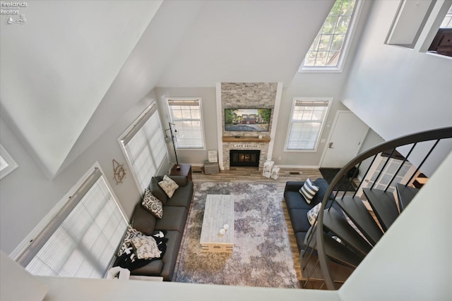 living room featuring a towering ceiling, wood-type flooring, a stone fireplace, and plenty of natural light