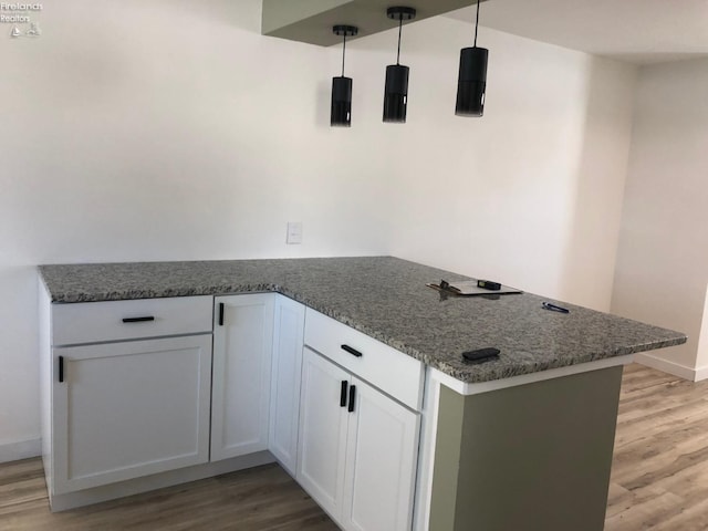 kitchen with white cabinetry, decorative light fixtures, kitchen peninsula, and dark stone counters