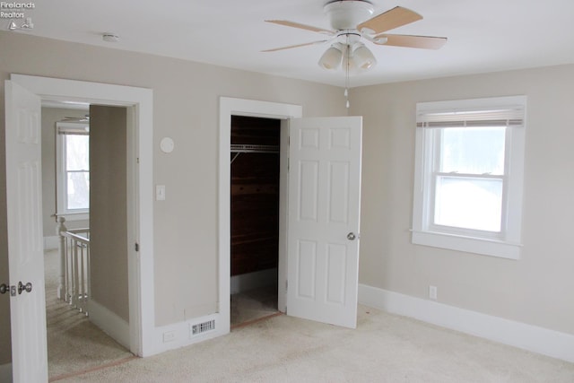 unfurnished bedroom with ceiling fan, light colored carpet, a closet, and a walk in closet