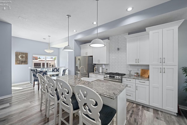 kitchen featuring stainless steel appliances, an island with sink, hanging light fixtures, and white cabinets