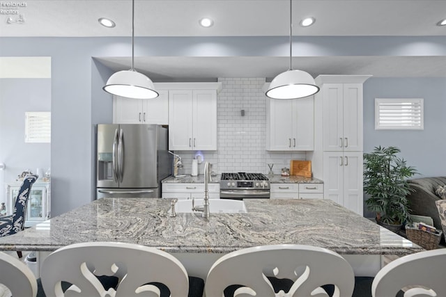 kitchen with white cabinets, backsplash, hanging light fixtures, stainless steel appliances, and a center island with sink