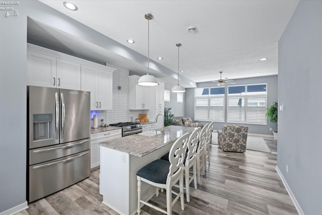 kitchen with stainless steel appliances, an island with sink, white cabinets, and light stone counters