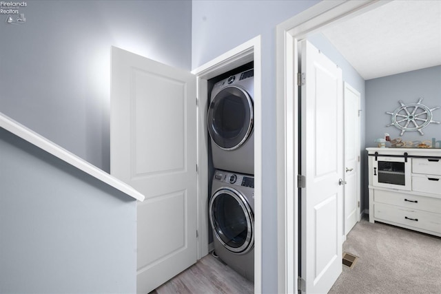 clothes washing area featuring stacked washing maching and dryer and light carpet