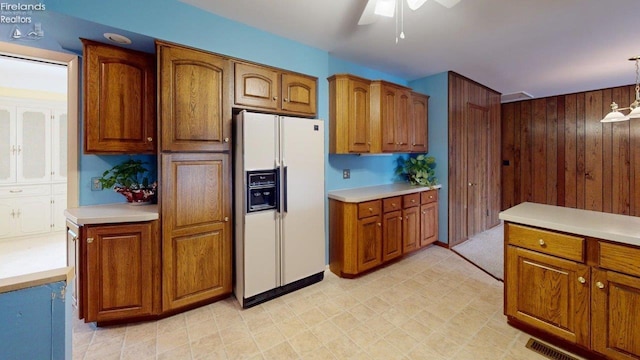 kitchen with ceiling fan, white fridge with ice dispenser, wooden walls, and decorative light fixtures