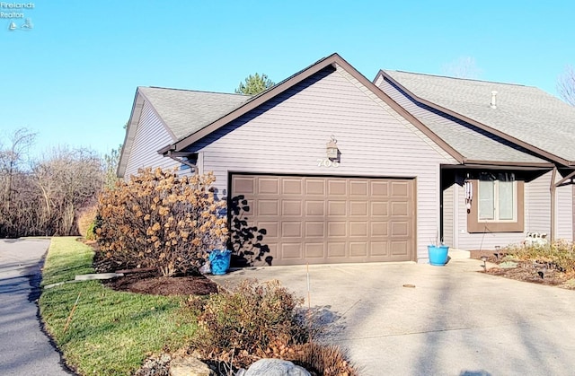 view of side of home with a garage, concrete driveway, and roof with shingles