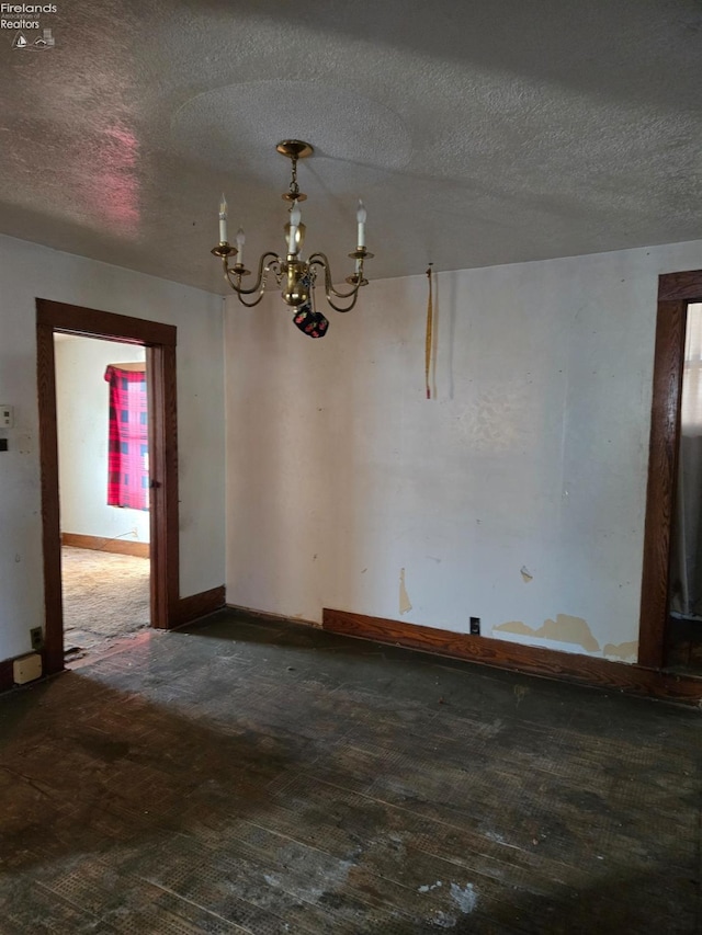 empty room with dark wood-type flooring, a textured ceiling, and an inviting chandelier