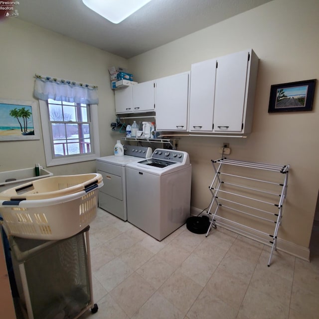 clothes washing area featuring light tile patterned floors, washing machine and dryer, and cabinets