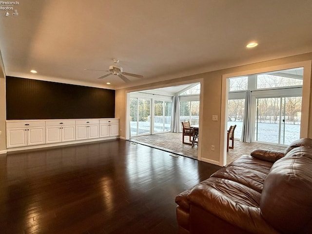 living room with a wealth of natural light, dark wood-type flooring, and ceiling fan