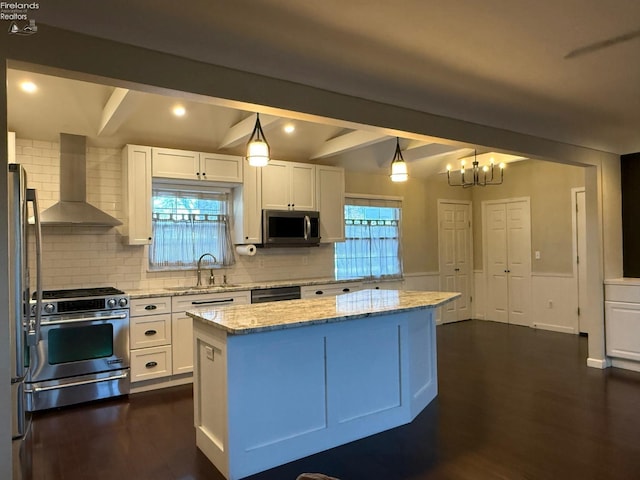 kitchen featuring wall chimney range hood, decorative light fixtures, stainless steel appliances, and a kitchen island