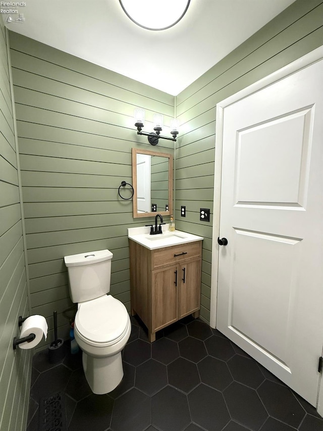 bathroom with tile patterned flooring, vanity, wooden walls, and toilet