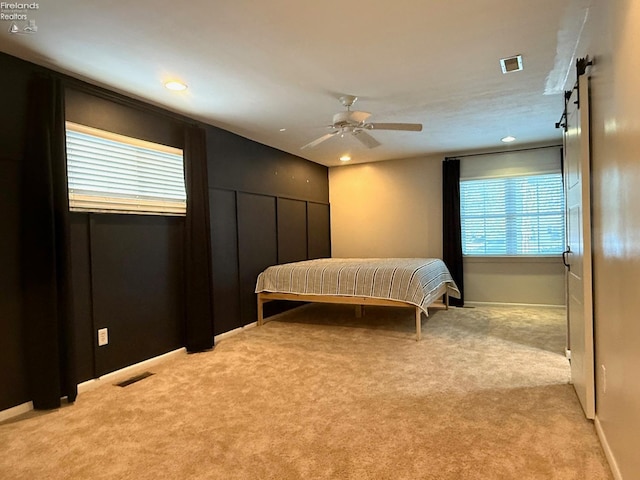 bedroom with light colored carpet, a barn door, and ceiling fan