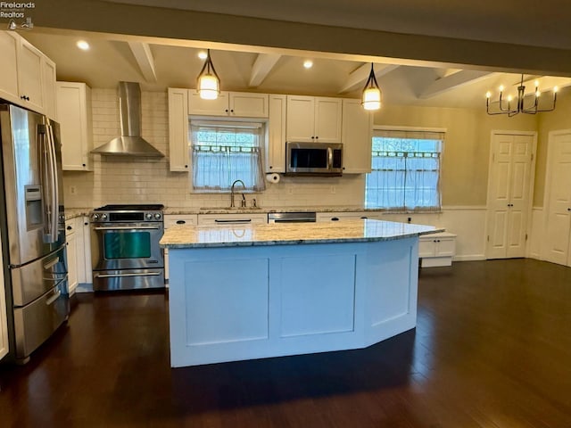 kitchen featuring pendant lighting, appliances with stainless steel finishes, beam ceiling, a center island, and wall chimney exhaust hood