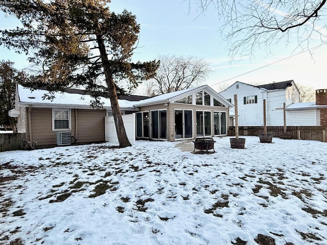 snow covered rear of property with an outdoor fire pit and a sunroom