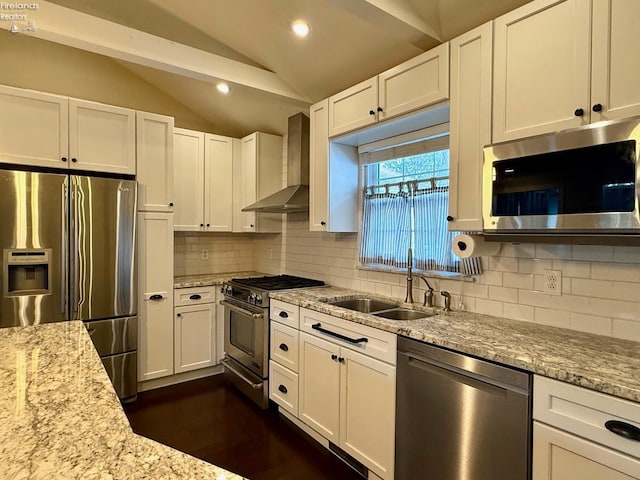 kitchen with vaulted ceiling, appliances with stainless steel finishes, sink, white cabinets, and wall chimney range hood