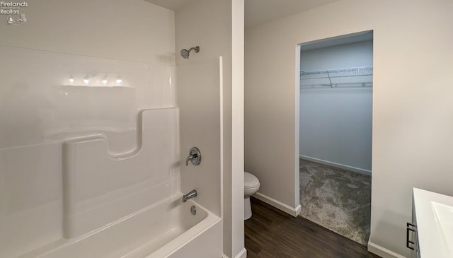 bathroom with hardwood / wood-style flooring, washtub / shower combination, and toilet