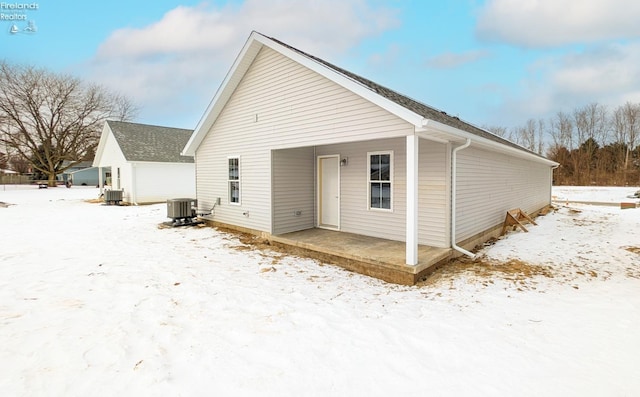 snow covered rear of property featuring central AC