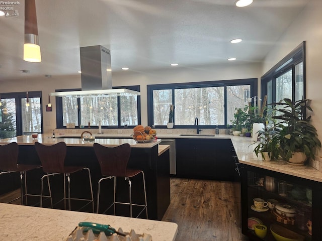 kitchen featuring sink, island range hood, dark hardwood / wood-style floors, pendant lighting, and light stone countertops