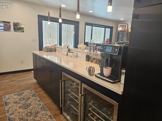 kitchen with light stone counters, decorative light fixtures, light hardwood / wood-style flooring, and beverage cooler