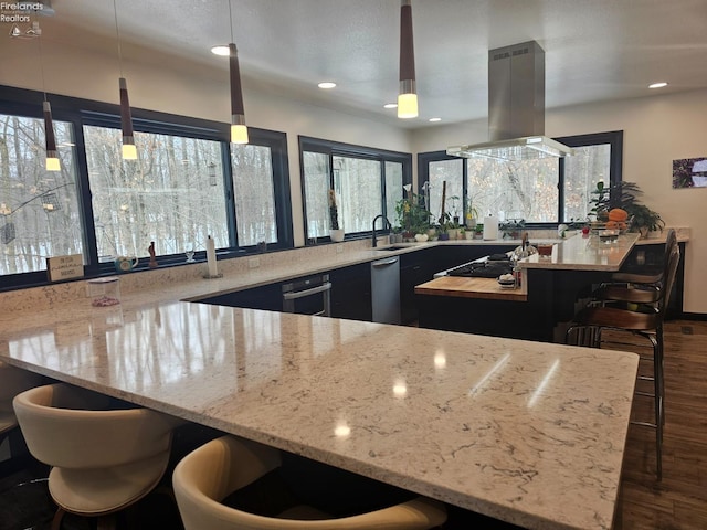 kitchen with pendant lighting, island exhaust hood, a kitchen breakfast bar, and stainless steel gas cooktop