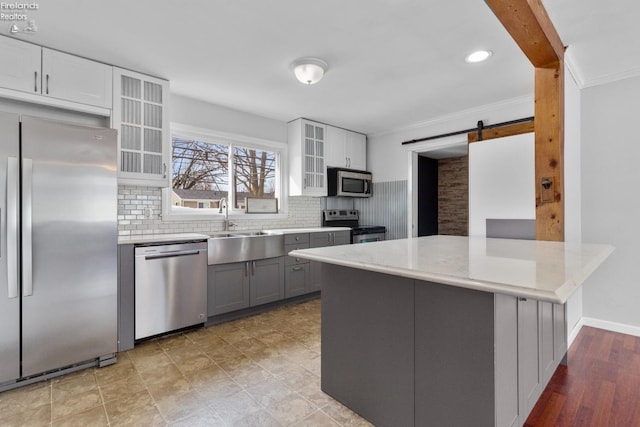 kitchen with sink, appliances with stainless steel finishes, white cabinetry, kitchen peninsula, and a barn door