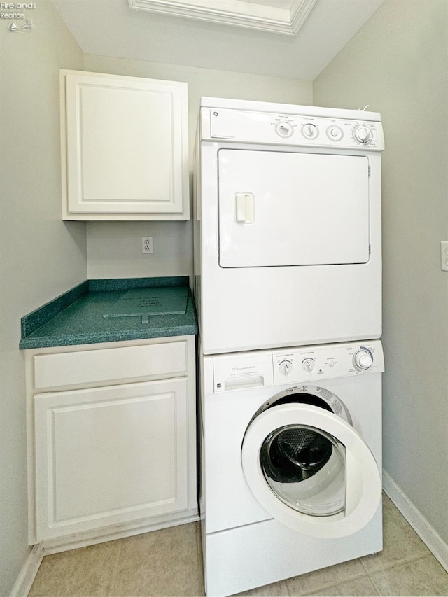 clothes washing area featuring cabinets, light tile patterned floors, and stacked washer and clothes dryer