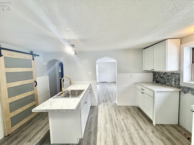 kitchen featuring sink, white cabinets, a barn door, a center island with sink, and light wood-type flooring