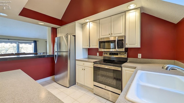 kitchen with lofted ceiling, sink, light tile patterned floors, white cabinetry, and stainless steel appliances