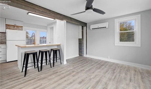 kitchen featuring a wall mounted AC, white cabinets, a kitchen breakfast bar, white refrigerator, and light hardwood / wood-style floors